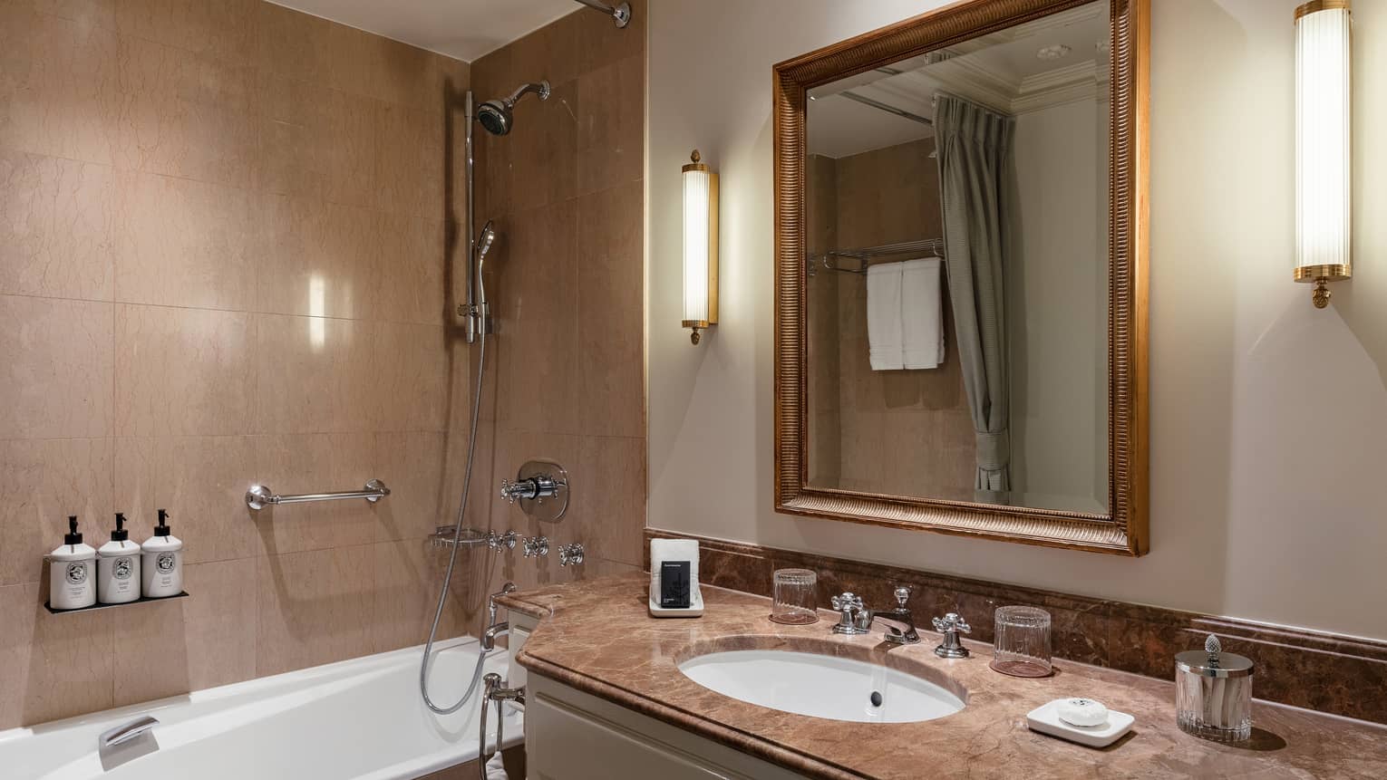 Luxury hotel bathroom with a marble countertop vanity, mirror, bathtub with a shower and wall-mounted toiletries