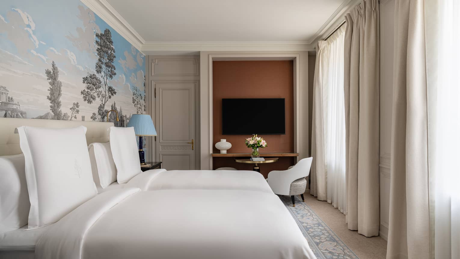 Hotel guest room with two beds, a light blue mural accent wall, TV and arm chair
