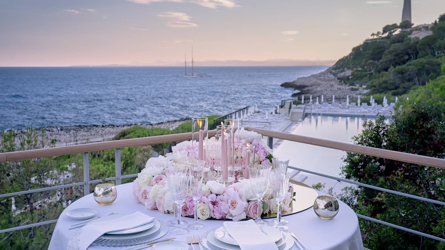Balcony with round set table, pink floral arrangement, water views at sunset