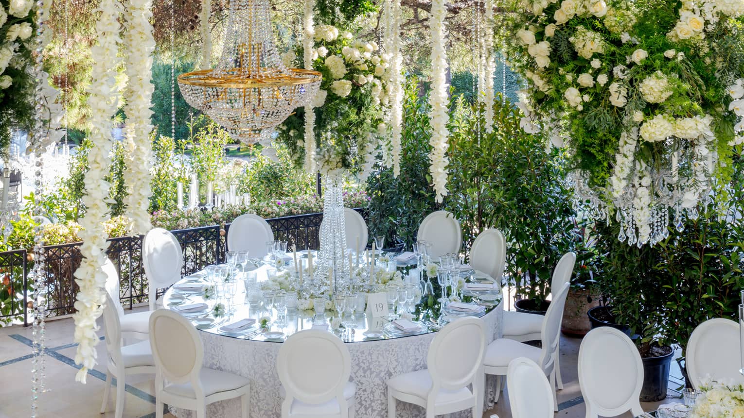 Round wedding banquet table on garden patio with chandelier, white flower garlands