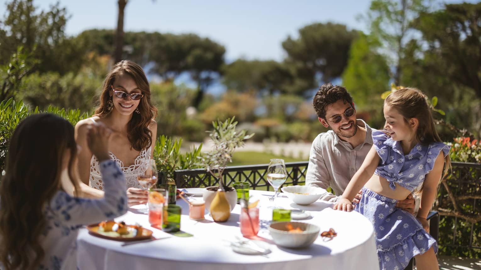 Family of four having a meal at a terrace table on a sunny day