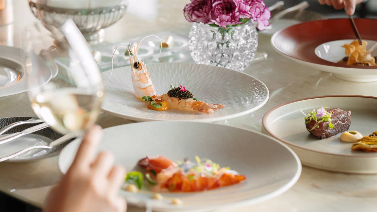 Fine dining dishes including prawns and filet on a dining table with purple flowers