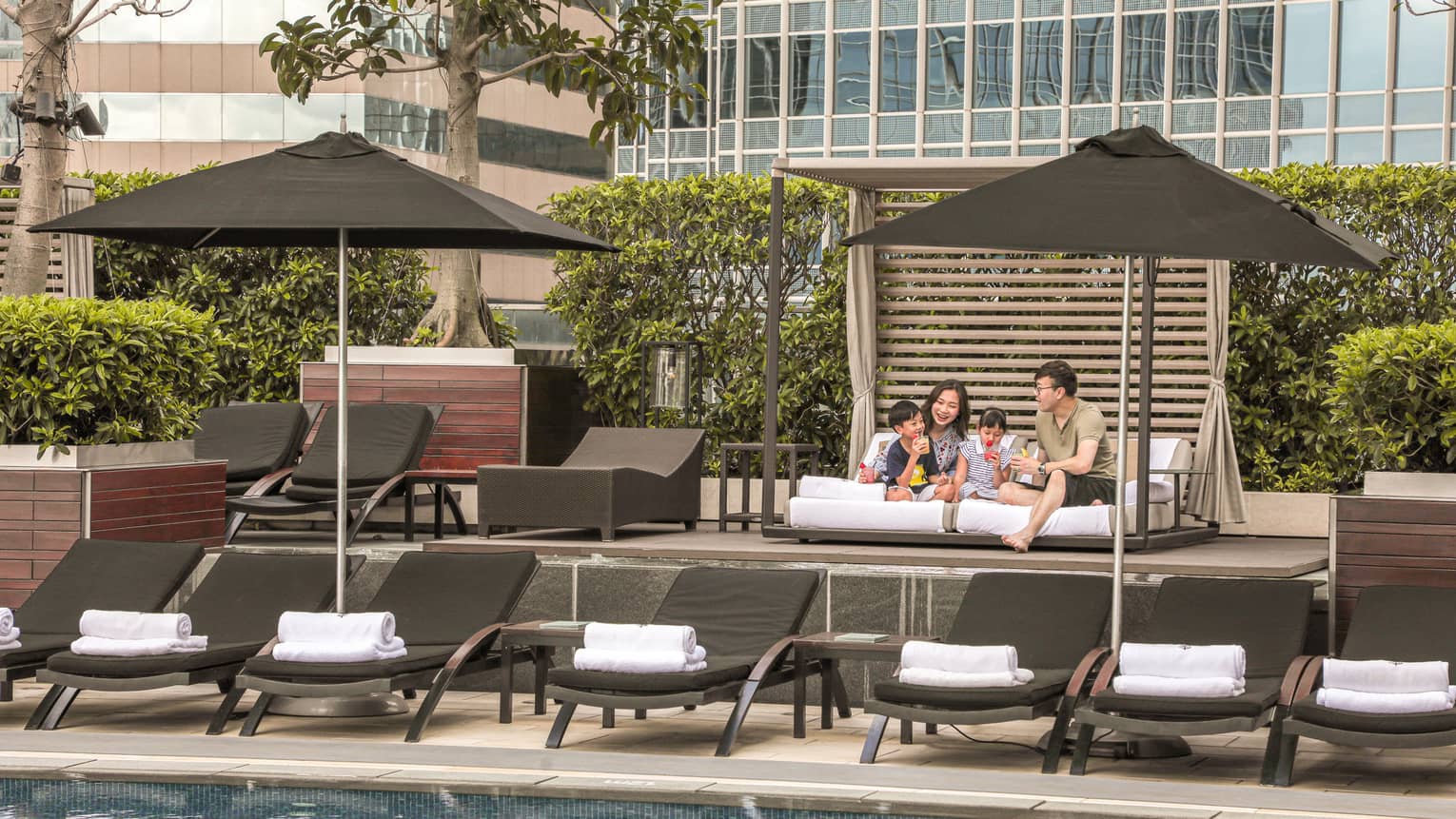 A mother, father and two young boys on daybed by pool
