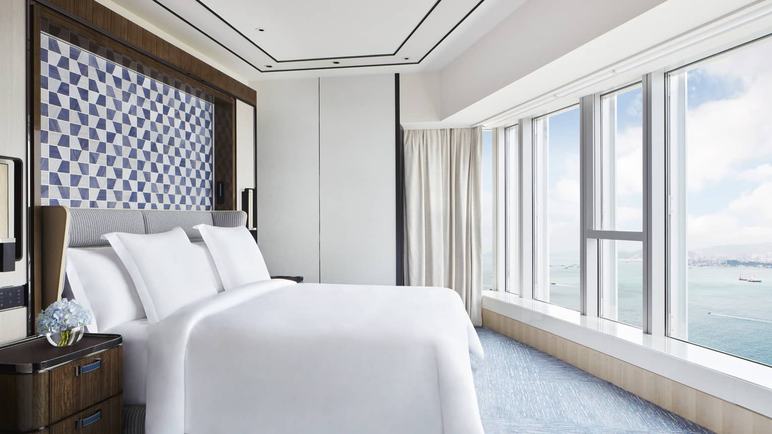 Bedroom with white king bed, checkered headboard and wall of windows