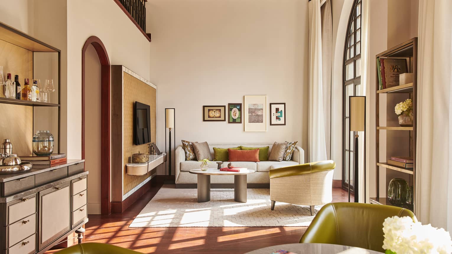 Hotel suite dining area in forefront, dry bar on left and neutral living room at far end with tall windows and long curtains
