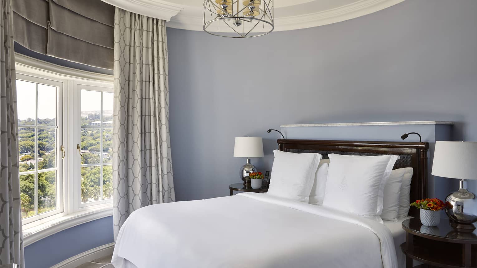 Hotel suite bedroom with king bed, circular ceiling with chandelier and crown molding, and window, at Four Seasons Hotel Johannesburg