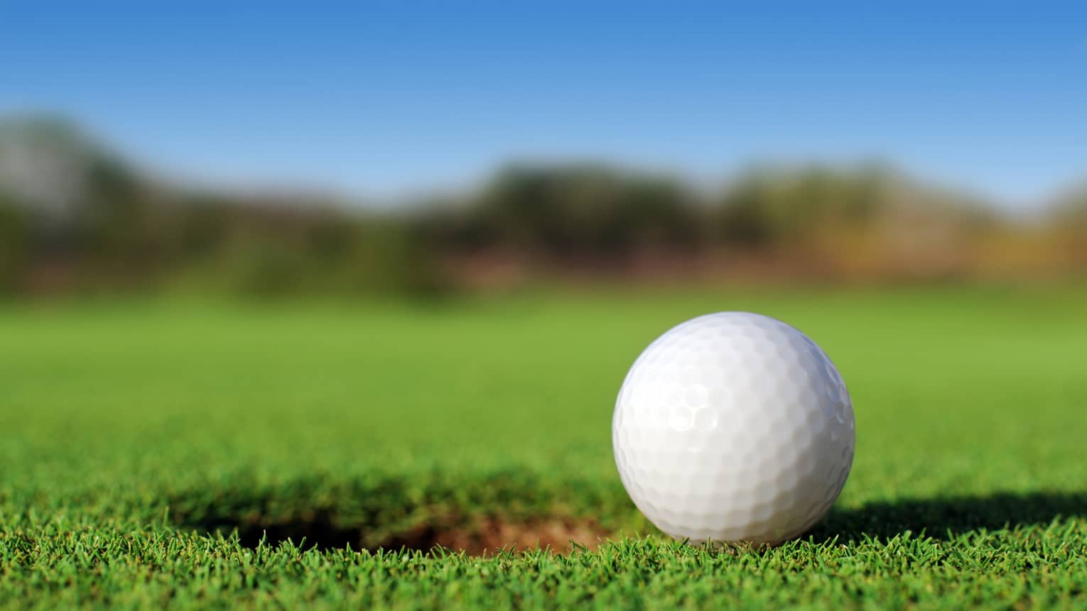 A close up of a white golf ball sitting right next to a golf hole on the course