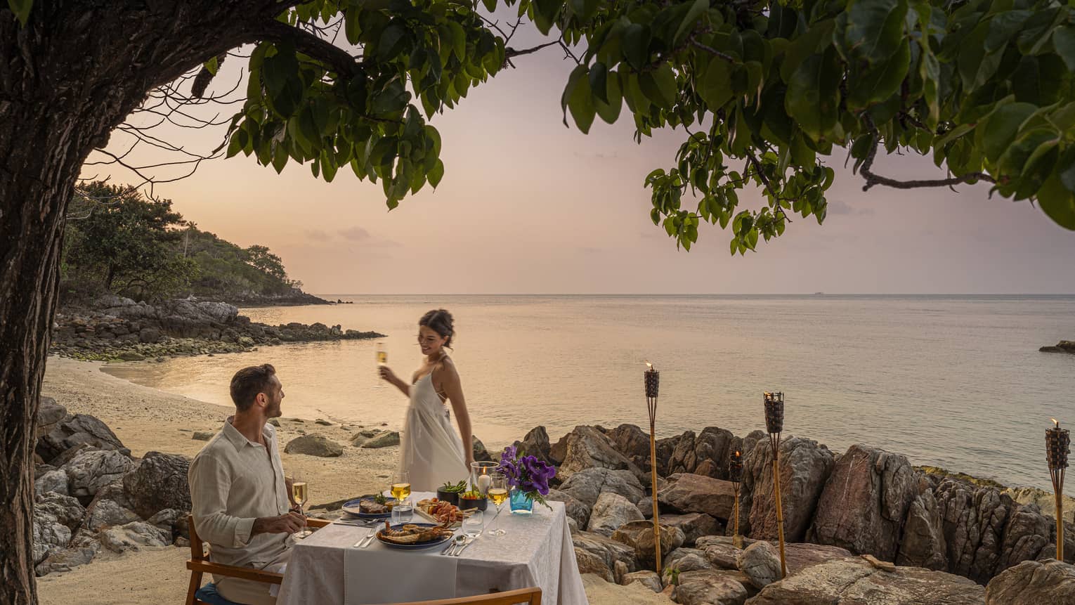 A beach dinner date at dusk, with a couple enjoying a serene seaside view.