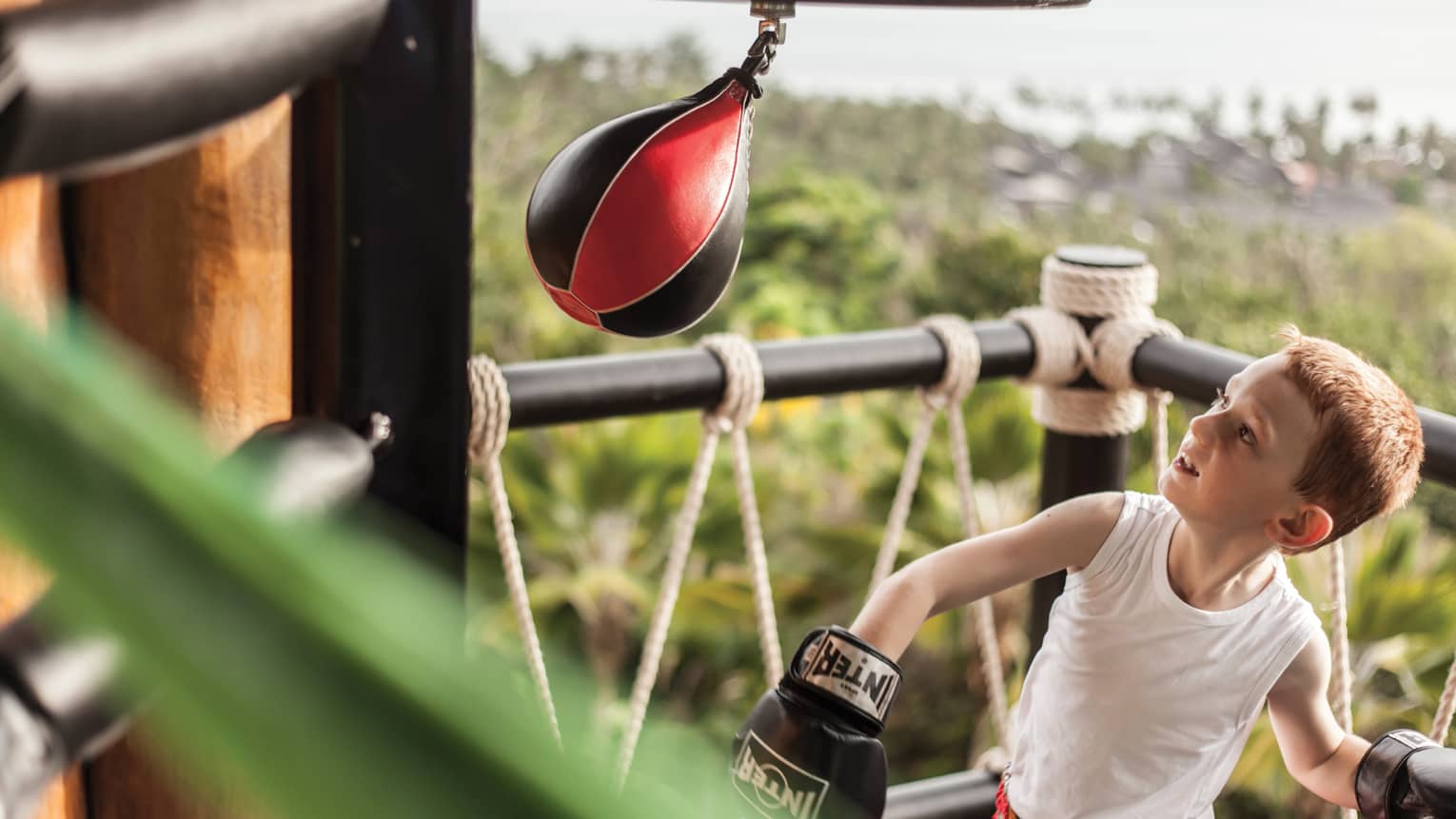 Young boy wearing boxing gloves in ring with small Muay Thai boxing bag