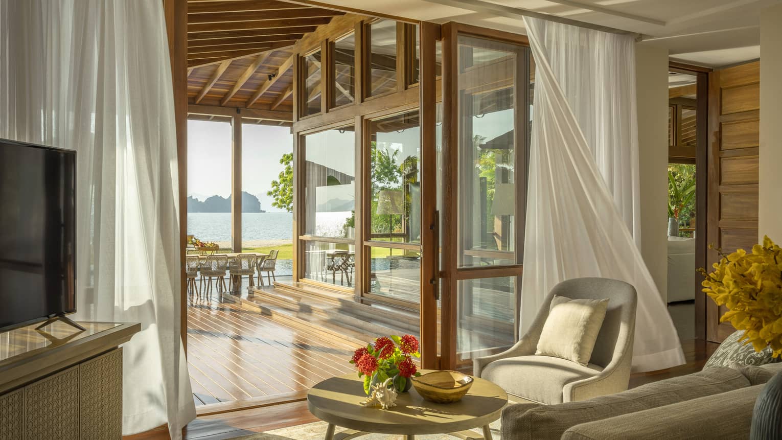 Sitting area opening up to covered wooden deck with beach view
