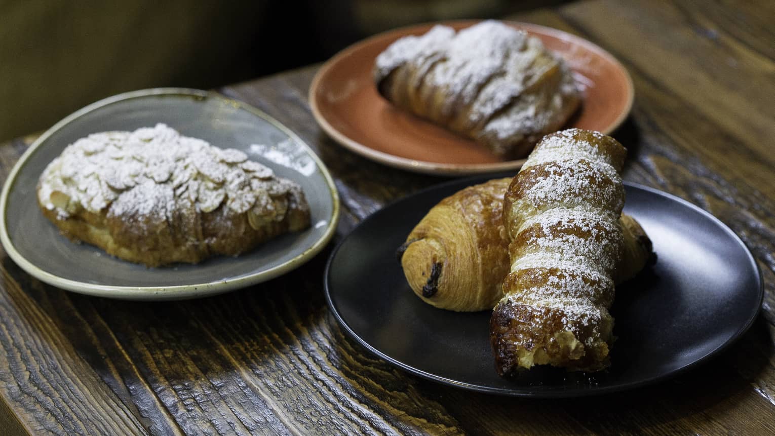 Four different croissants and pastries on a black, grey, and orange plate.