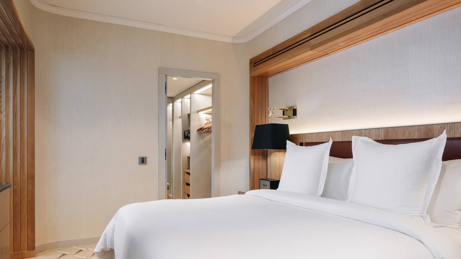 Hotel bedroom with white king bed, headboard wall with recessed lighting