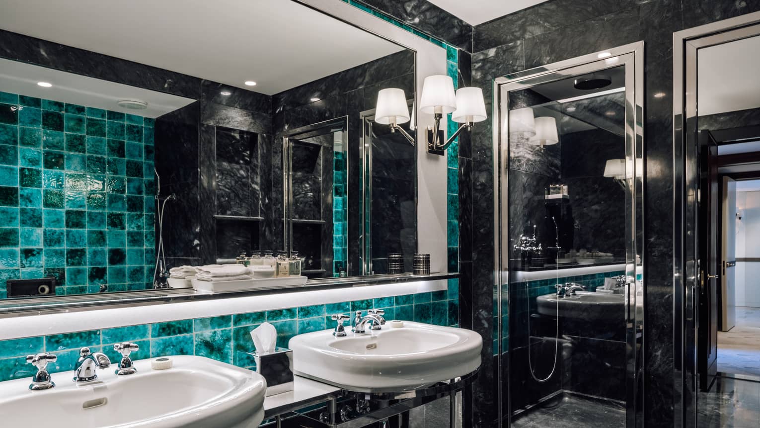 Luxurious bathroom with black marble walls, turquoise tiles, double sinks, a large mirror and a glass-enclosed shower.
