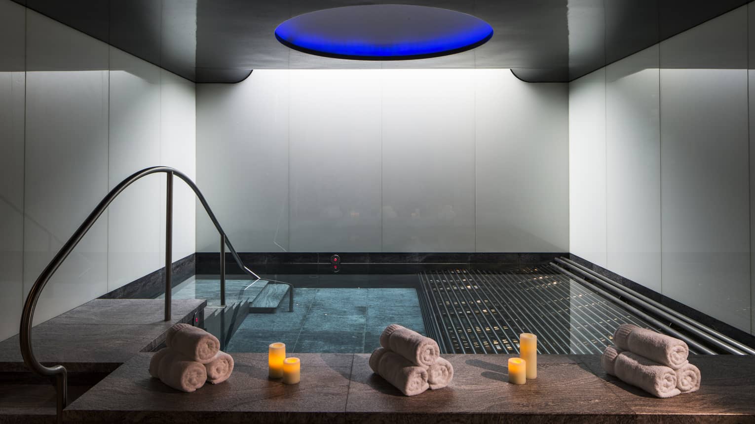 Rolled white towels, candles on spa vitality pool ledge under blue dome ceiling