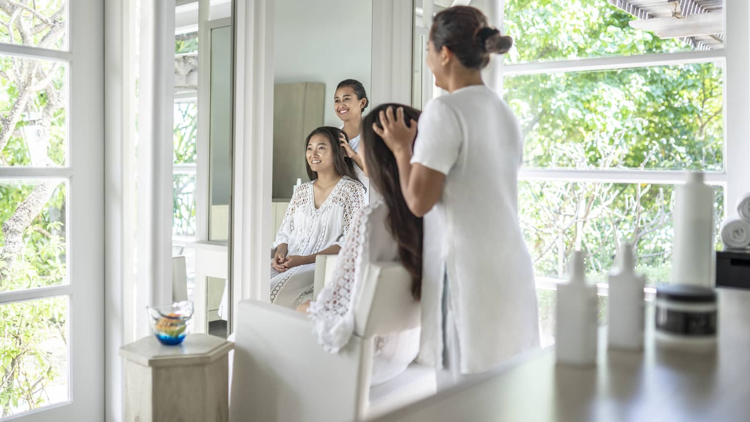 Person enjoying a hair treatment in a spa salon with large windows, surrounded by lush greenery