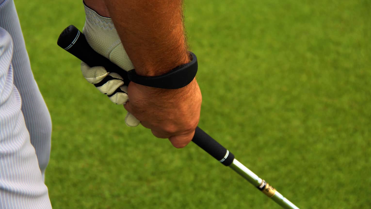 Close-up of hands gripping golf club on golf course green
