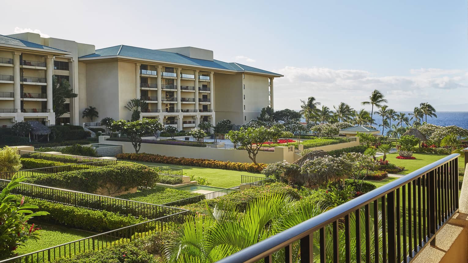 Balcony view of resort buildings with landscaped gardens, palm trees and ocean in the background