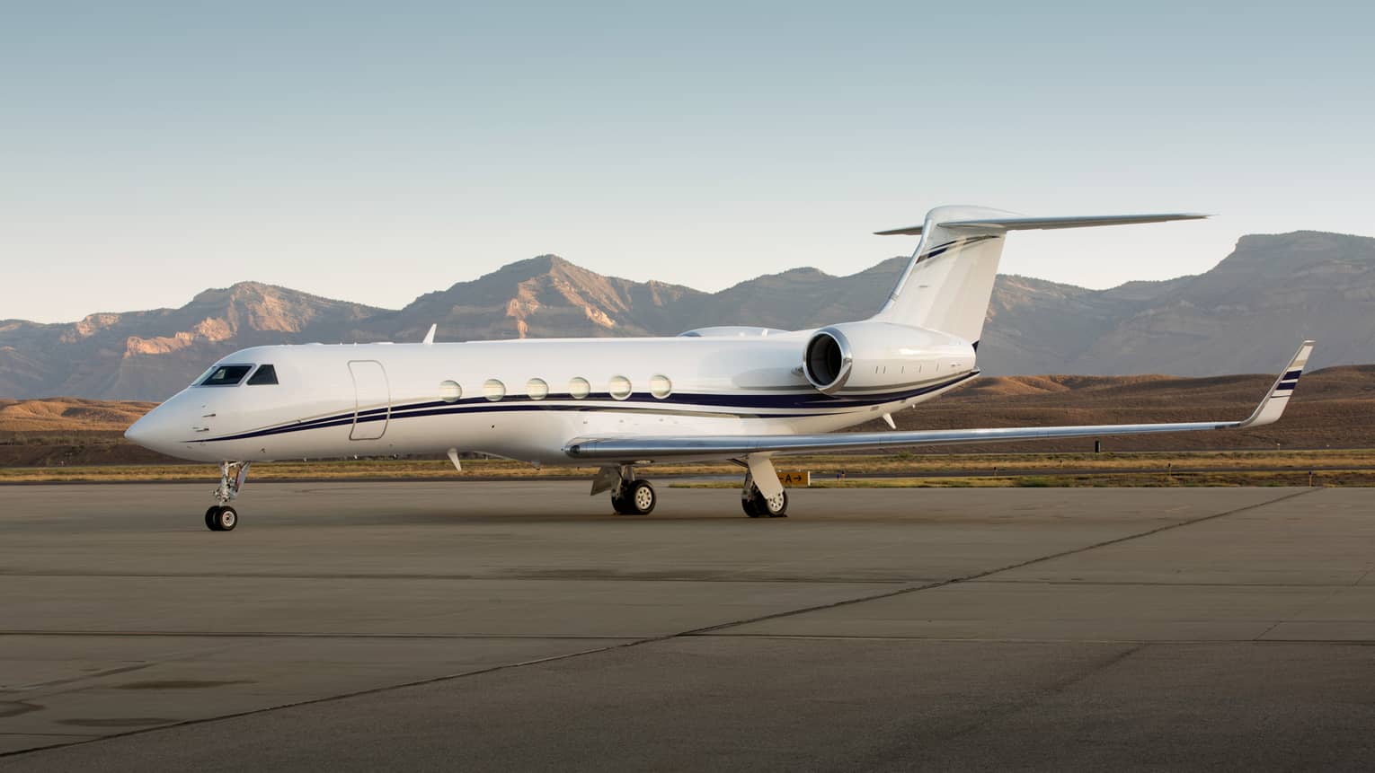 Private jet parked on a runway with mountain range in the background.