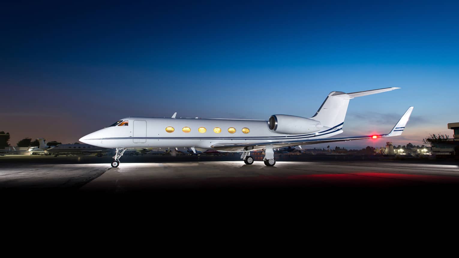 Jet Edge private jet parked on the tarmac at dusk with lights on inside, set against a clear blue sky