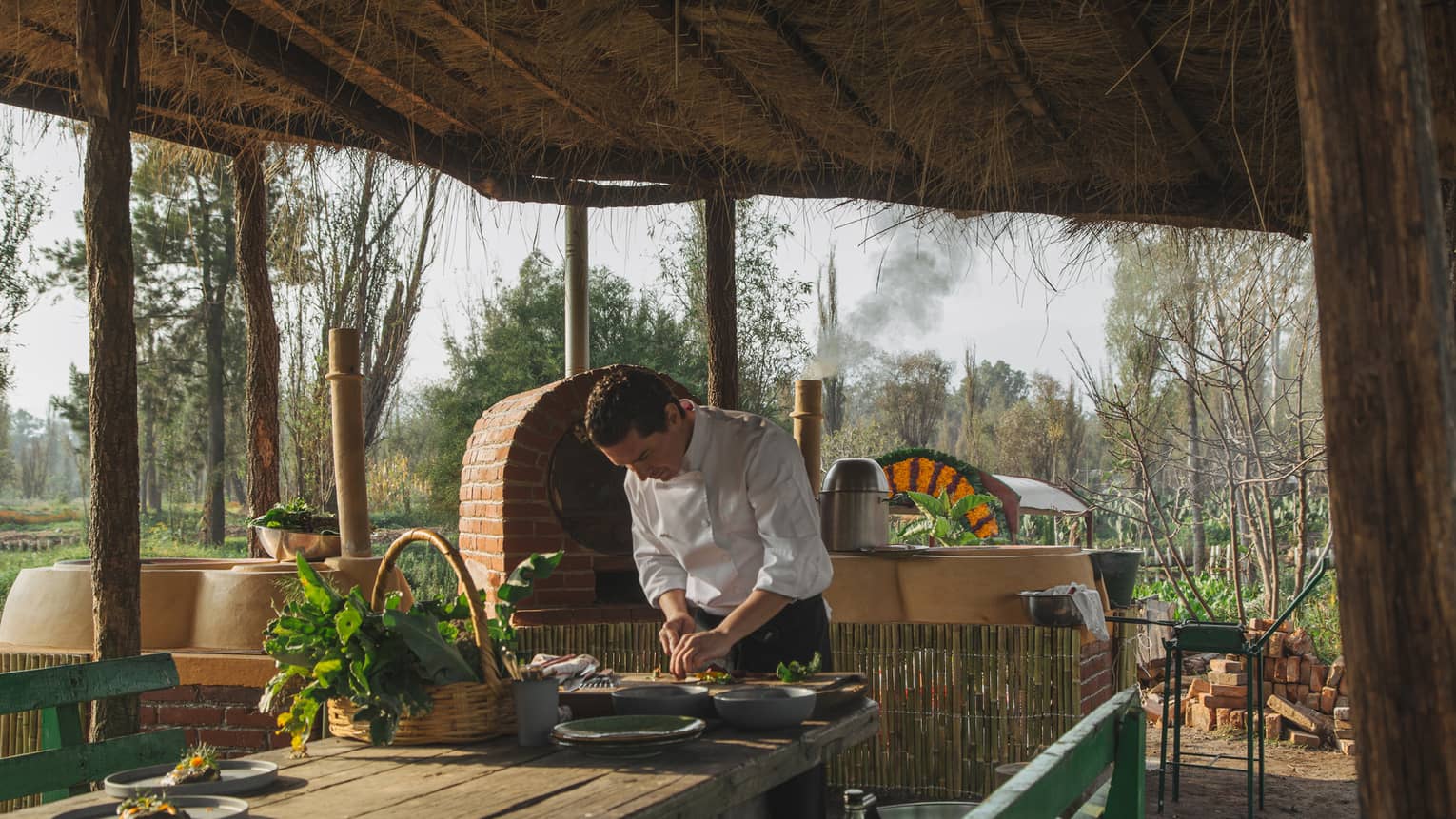 A chef chopping something with a knife outside on an old table, a roof made of old wood covers him.