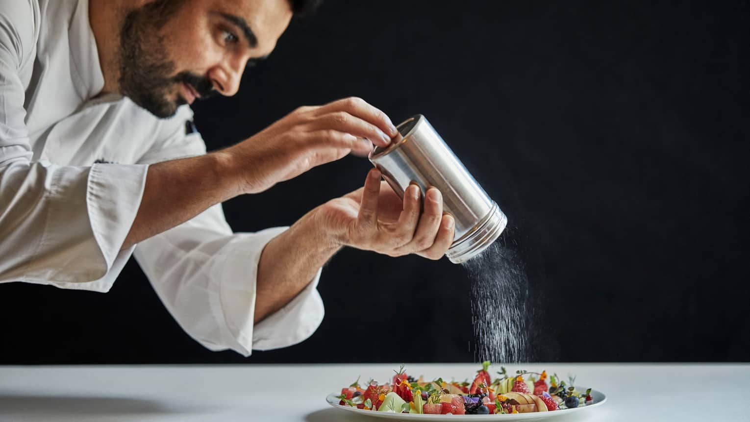 Executive Chef Antonio Mermolia shakes powdered sugar over plate of dessert 