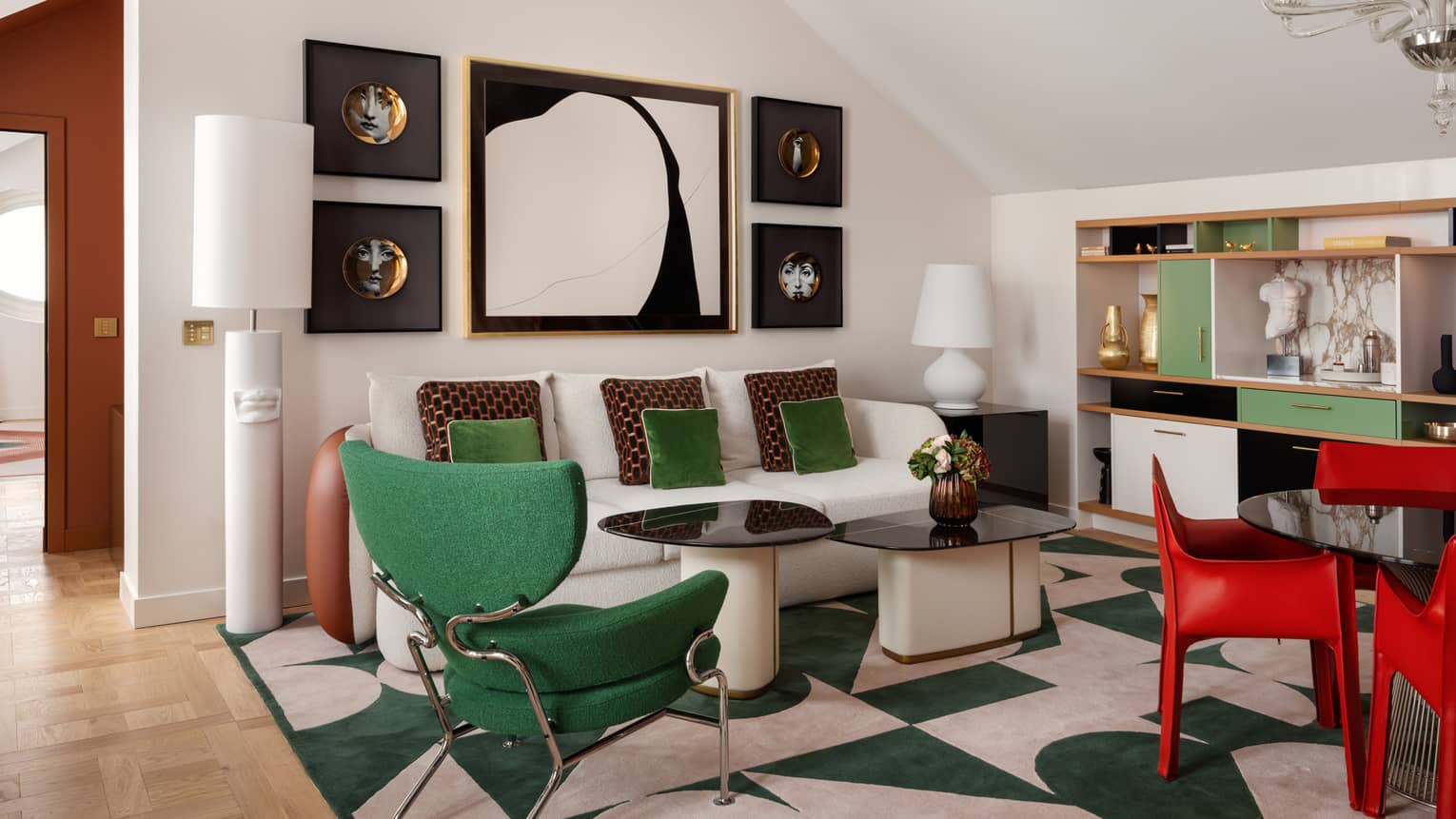 A stylish hotel suite sitting area with emerald-green accent pieces and bright red dining chairs