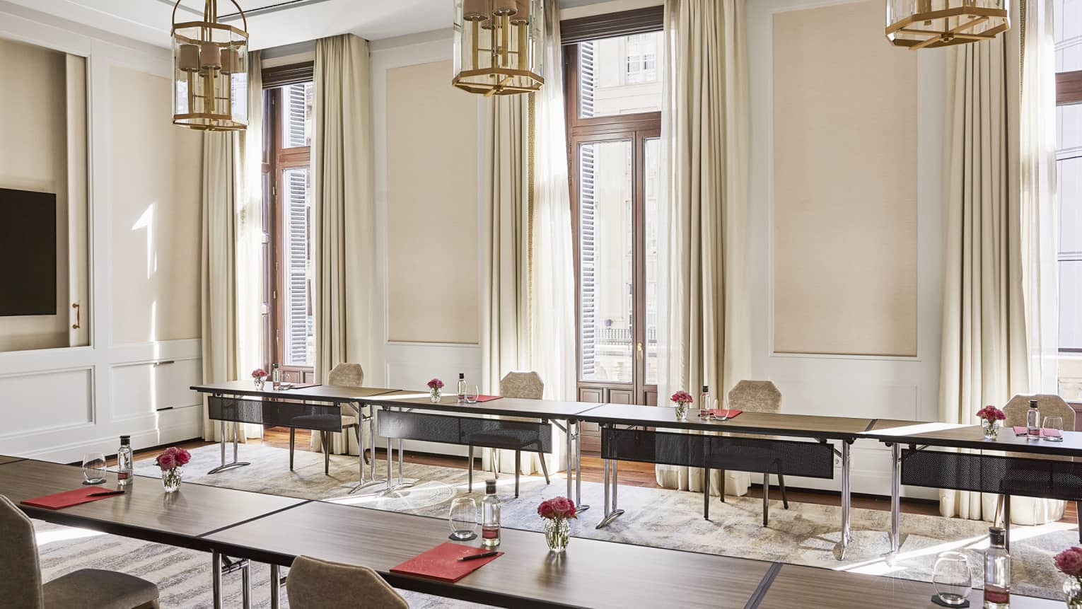Meeting room with u-shape table set-up, three small chandeliers hanging from ceiling, three windows