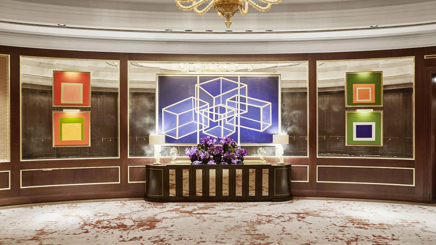 Sol Foyer with mirrored walls, colourful artwork, centre table with purple flowers, gold chandelier