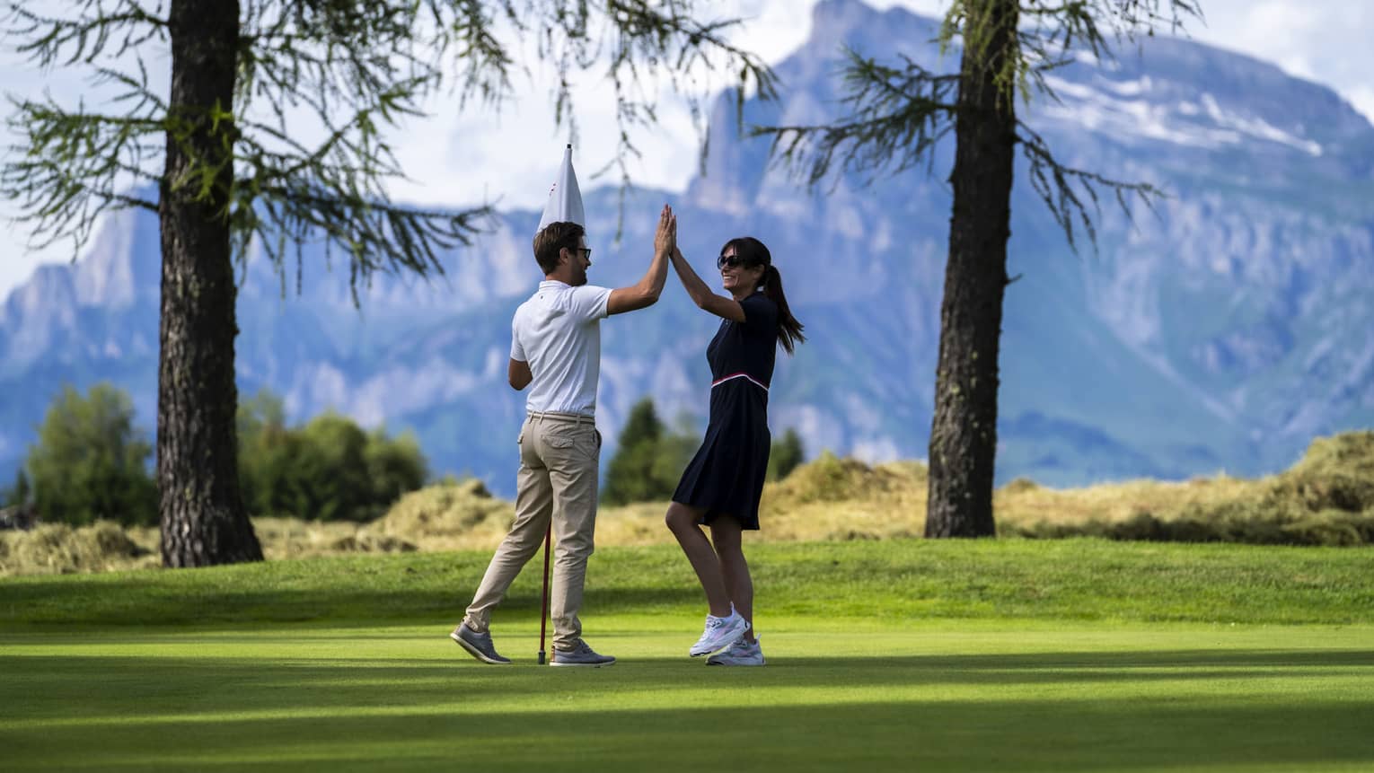 Two people high-fiving on a golf course with mountains in the distance