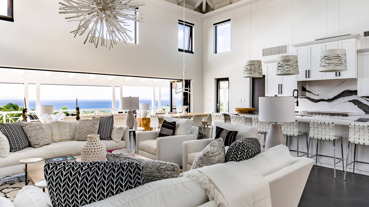 Large common area with long marble kitchen island, white living room furniture, sea view