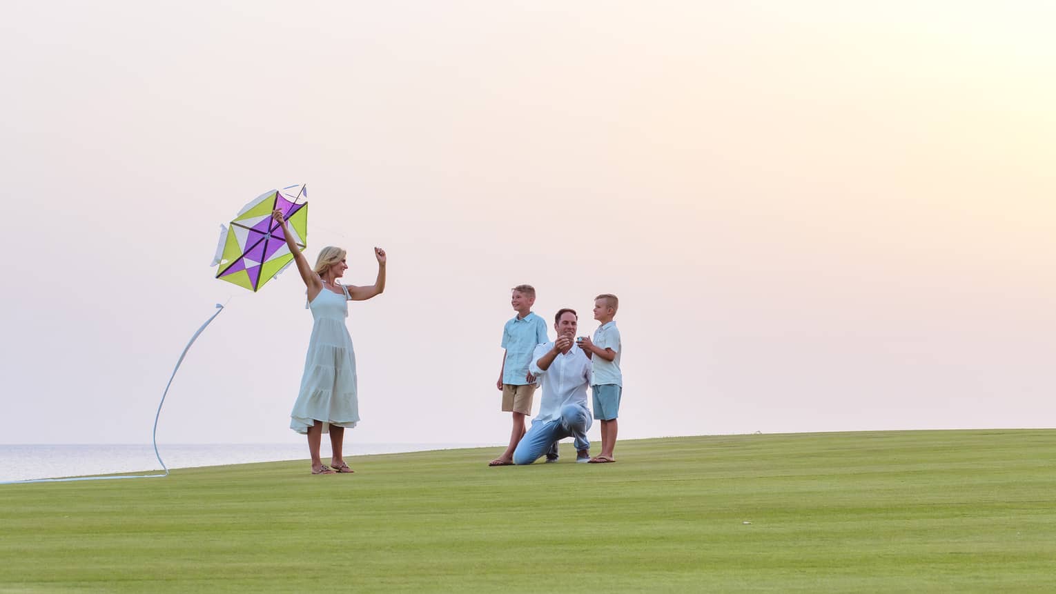 A family about to fly a kite while resting on green grass.