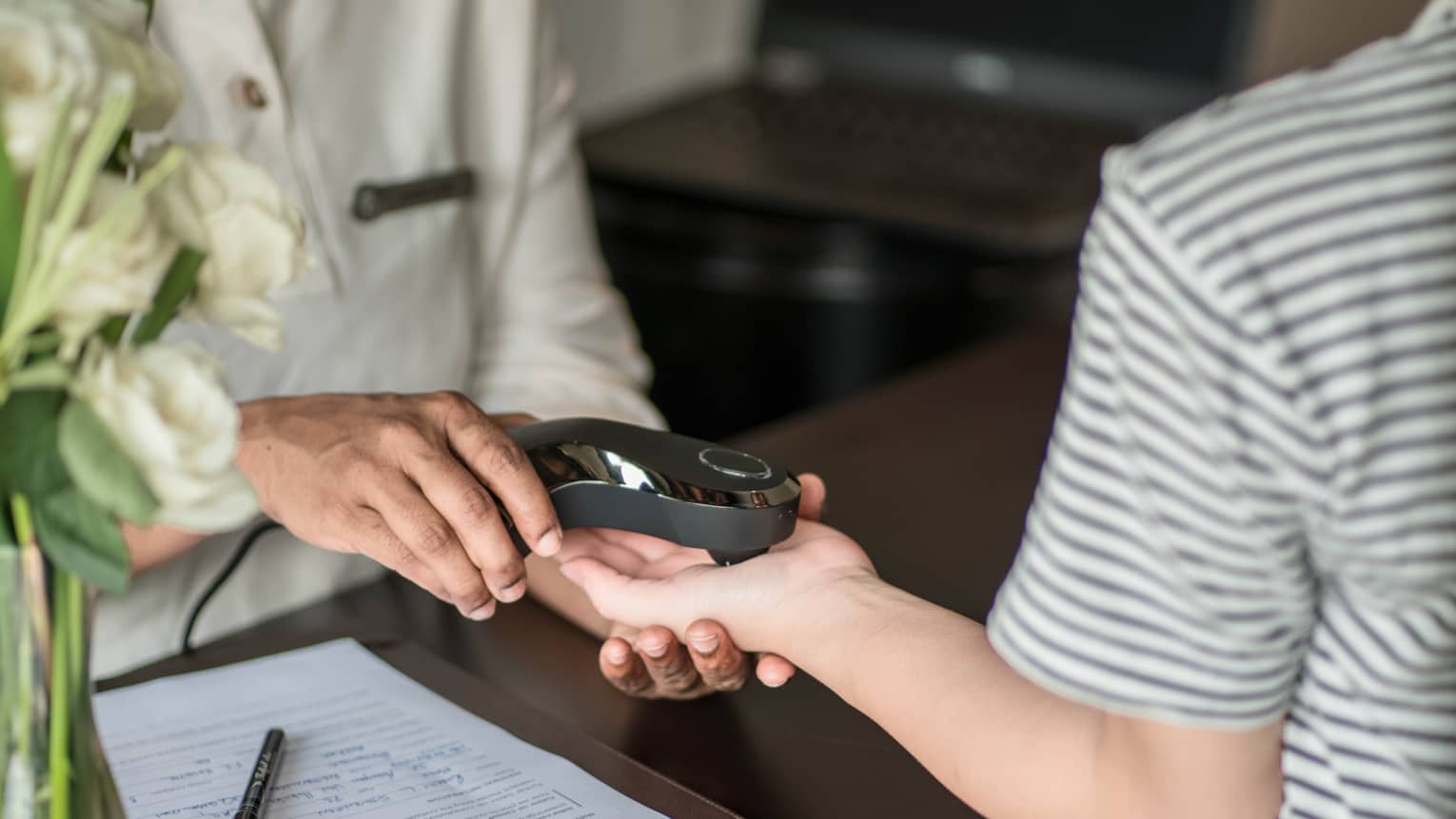 Close-up of a person receiving a spa treatment, with a therapist using a handheld device on their hand, alongside a clipboard with paperwork on the table.