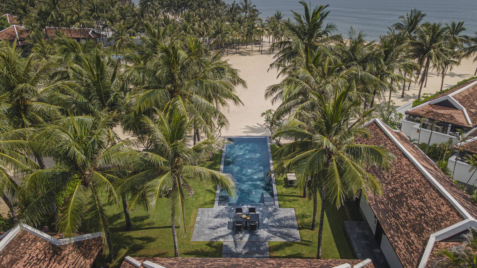 Aerial view of private beachfront villa with rectangular pool in tropical setting