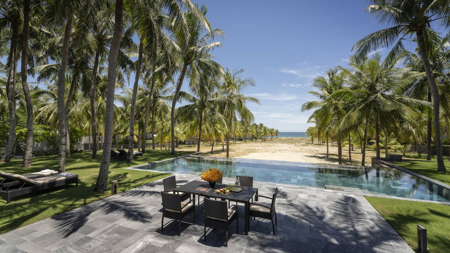Three-Bedroom Pool Villa pool area with dining table, lounge chairs, palm trees, ocean views