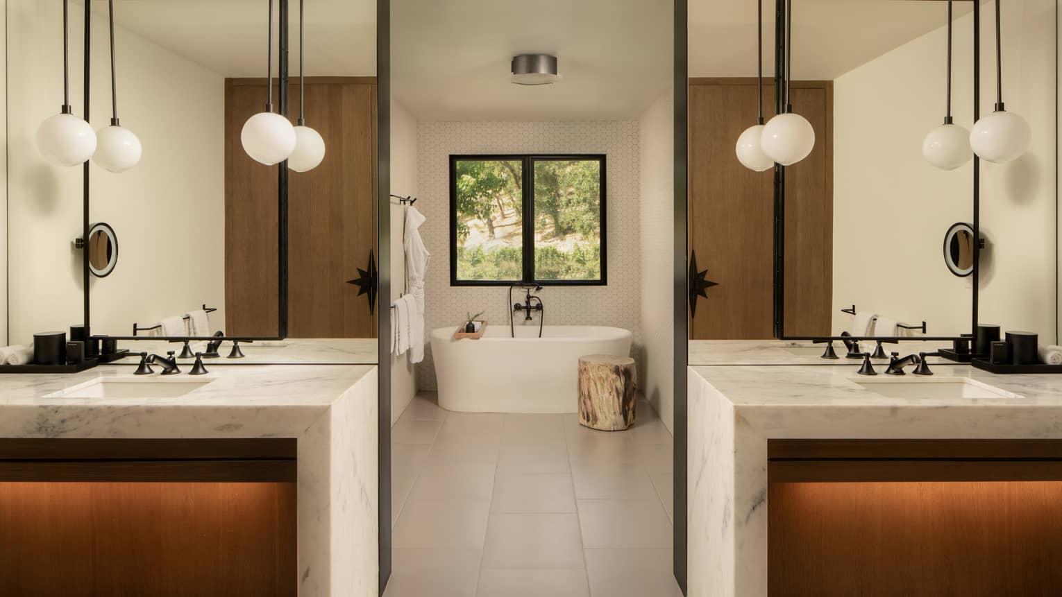 Contemporary bathroom featuring two separate marble vanities, each with opal pendant lights, and a walkway in the middle which leads to tub