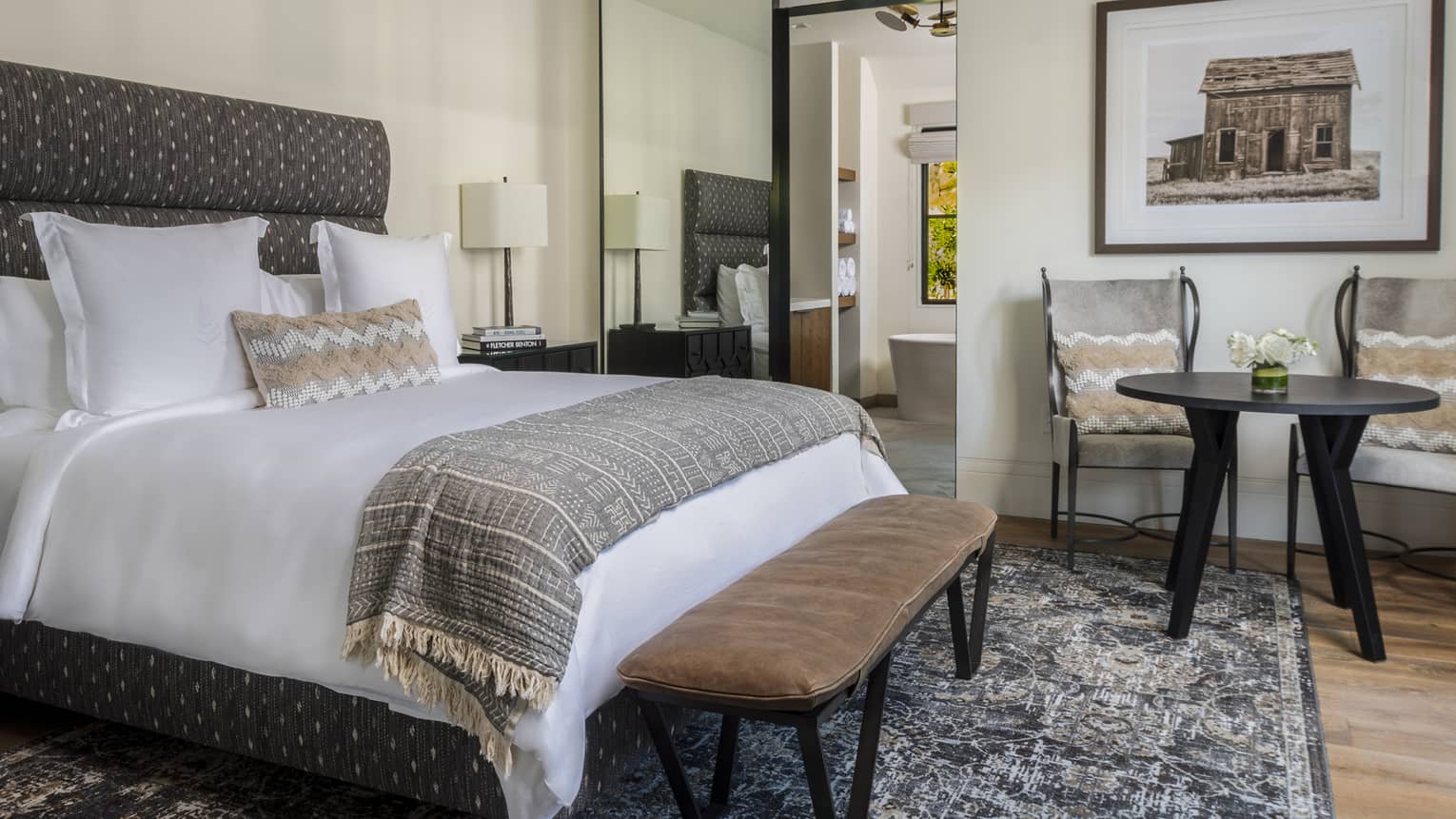 Bedroom with king bed, bench, table and two chairs and area rug