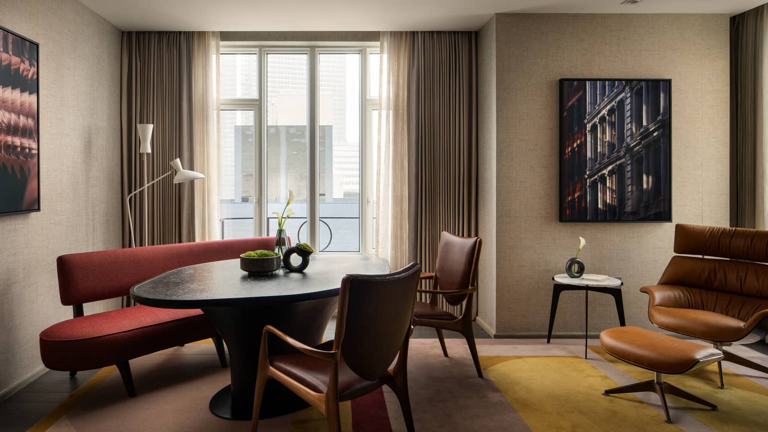 Luxury suite sitting area with a red bench, black oval table, brown leather chairs and floor-to-ceiling windows