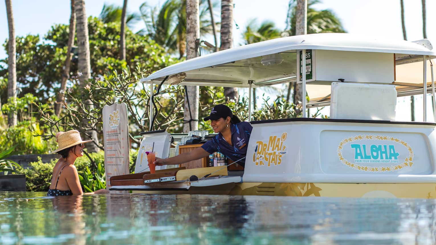 A woman serves a drink from a surfer van-inspired swim-up bar at resort pool