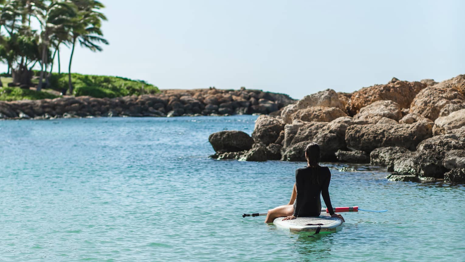 Person sits on stand-up paddleboard in a tropical lagoon