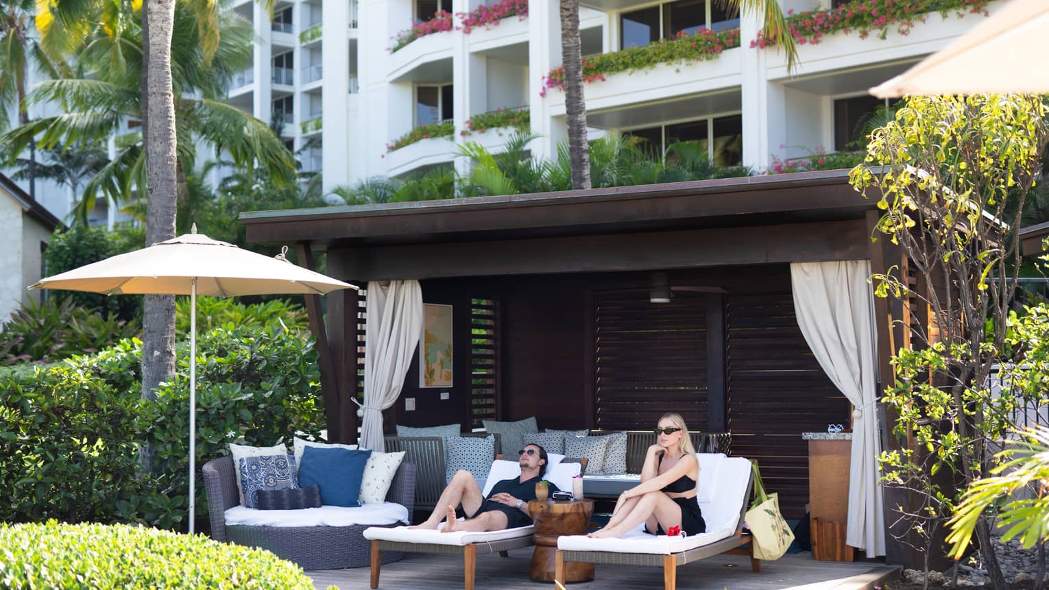 Man and woman lounge on sun chairs under private cabana