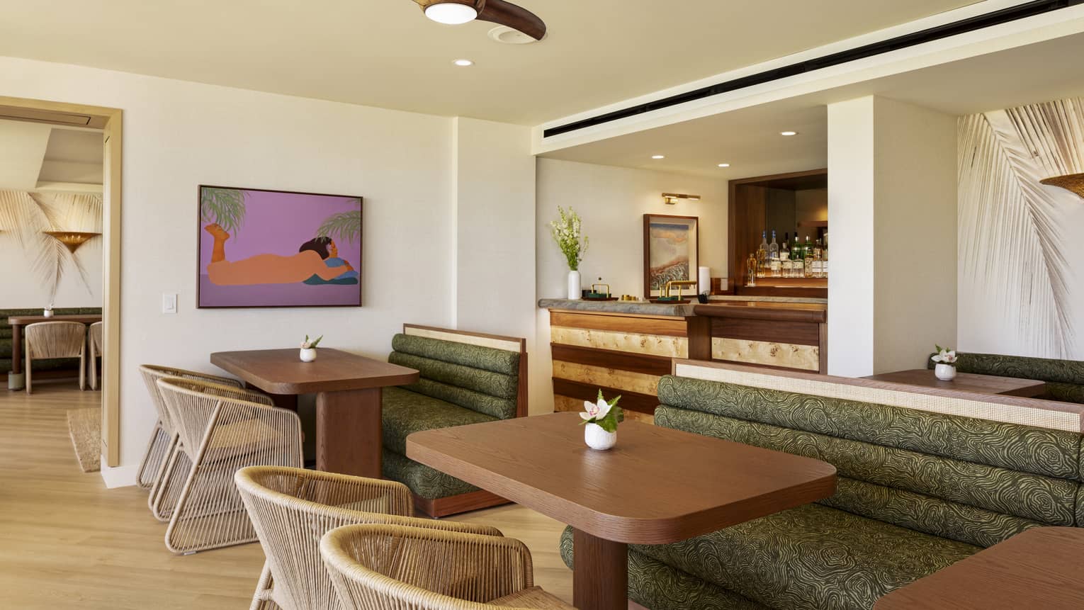 Wooden dining tables in an executive club lounge, featuring large green booths and woven beige chairs