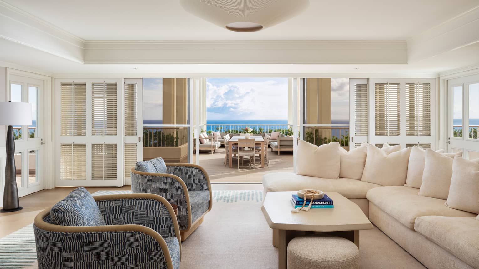 Luxury resort suite living room with plush furniture and opening to an ocean-view dining terrace