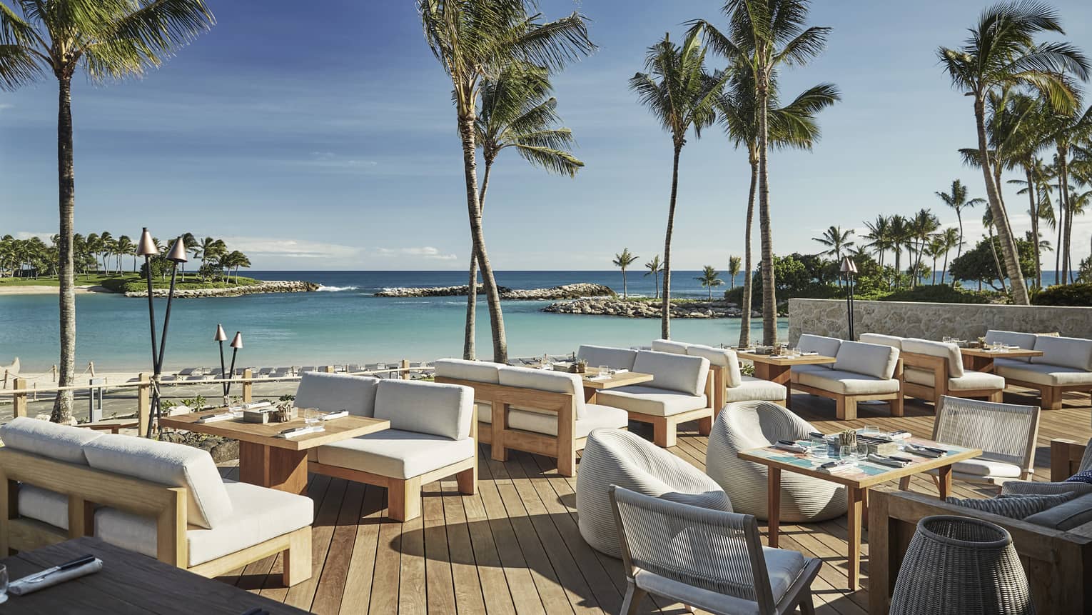 Plush white patio chairs around wood tables on sunny waterside Minas lounge