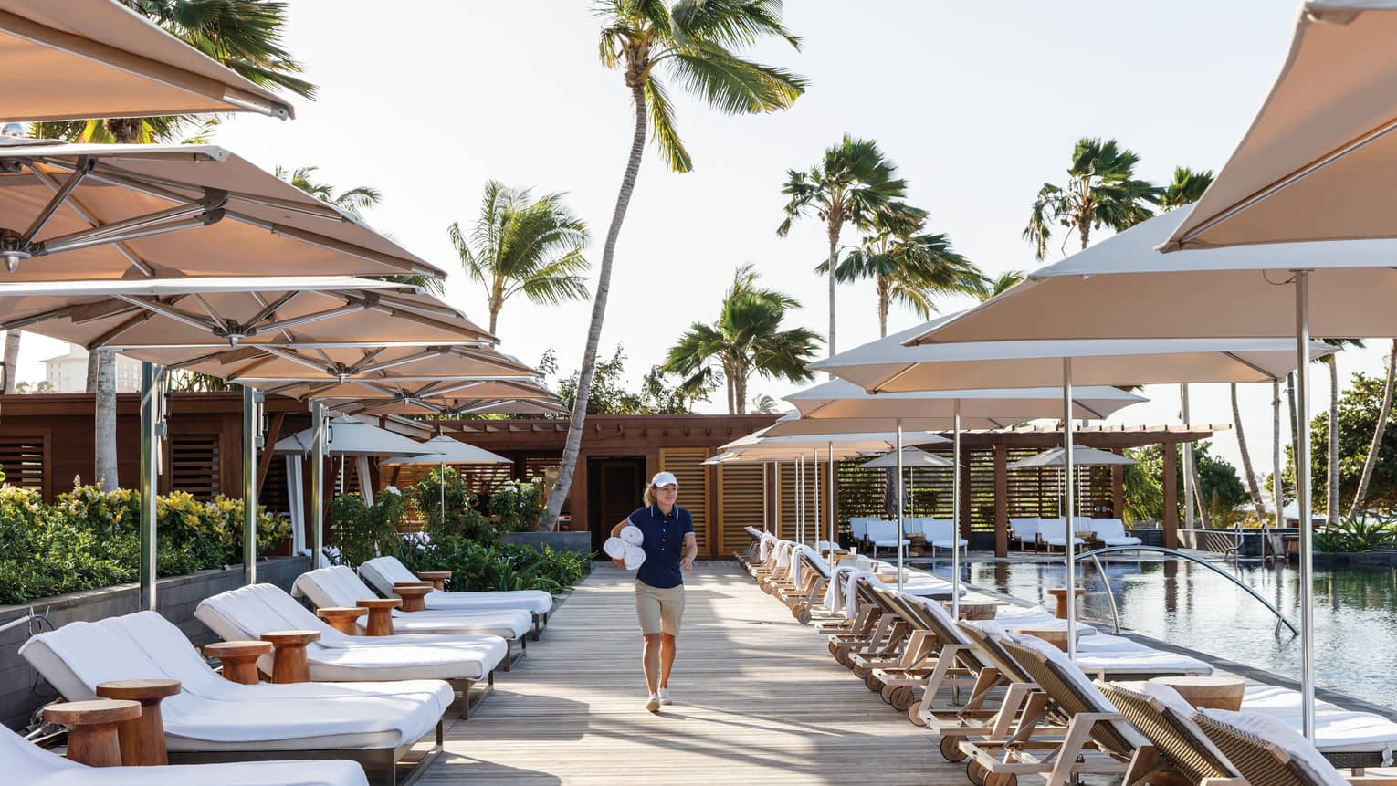 Hotel staff carries rolled white towels past lounge chairs on swimming pool deck