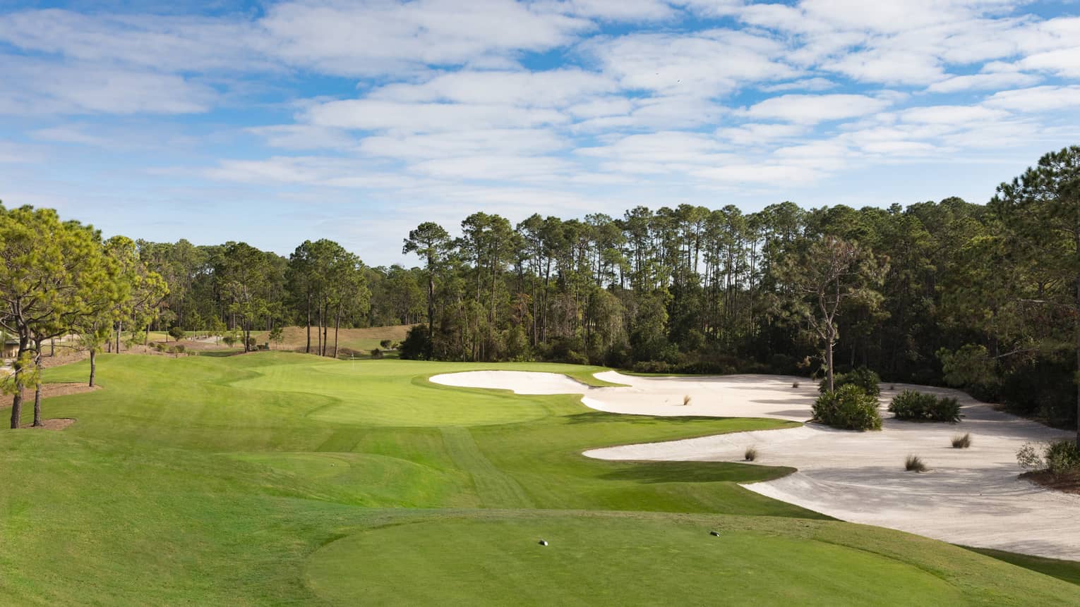 The sky is blue over a green golf course with sand dunes