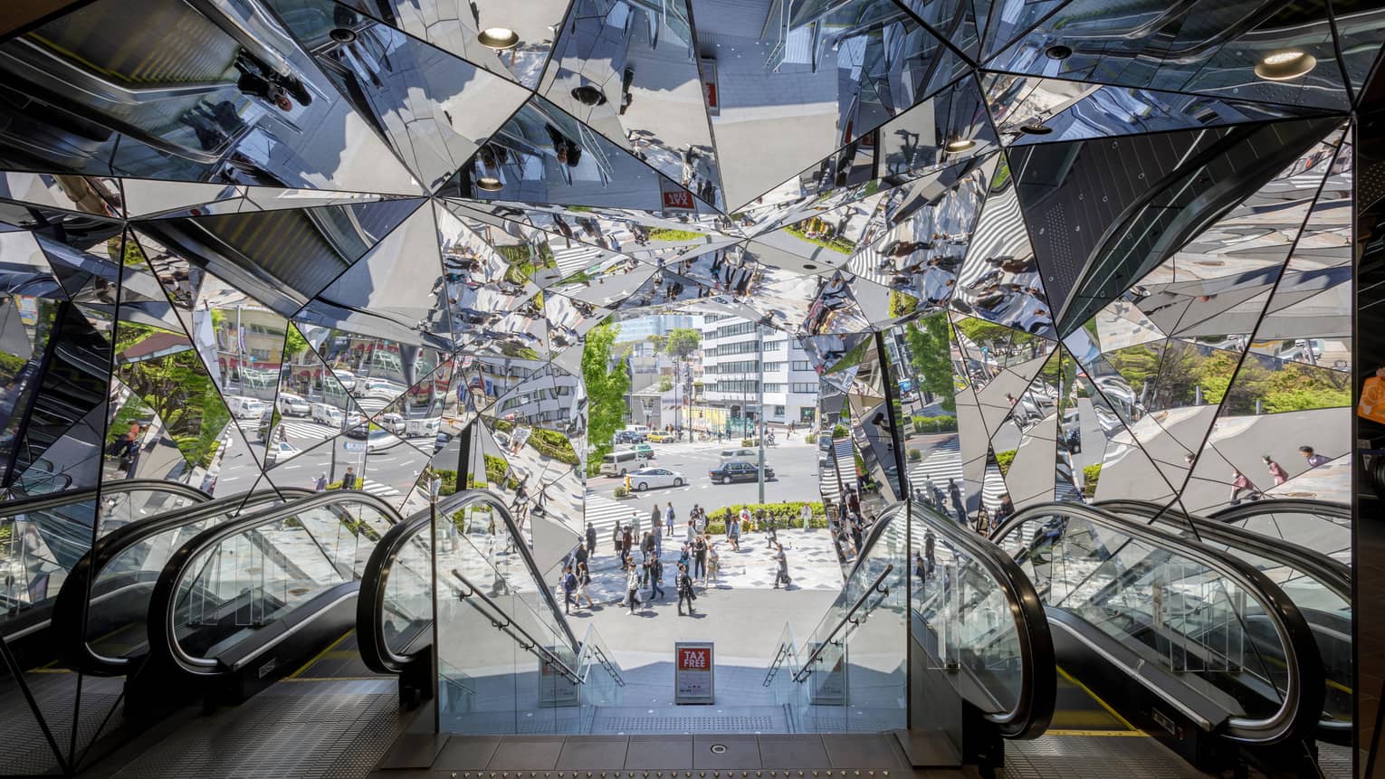 Escalators leading to a mirrored entrance reflecting pedestrians and a busy street scene