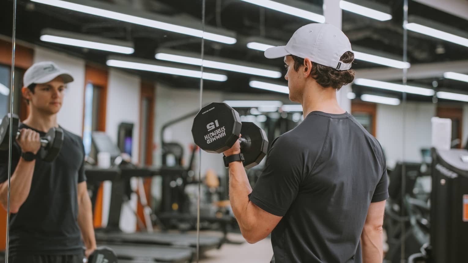 Person at a gym and standing in front of a mirror lifting weights.