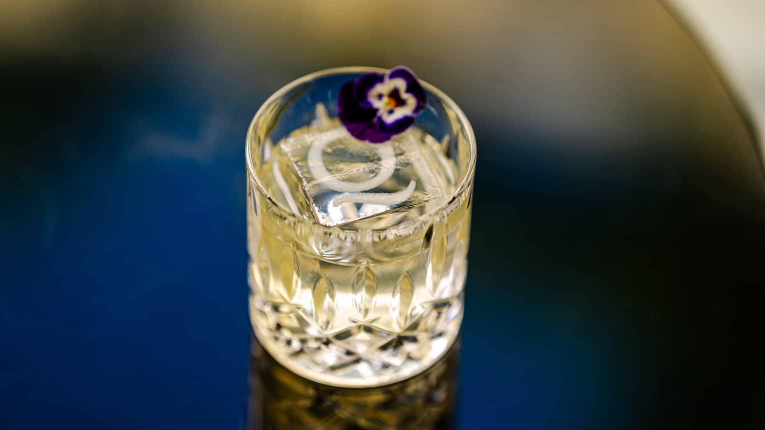 A drinking glass with ice cubes and an edible flower