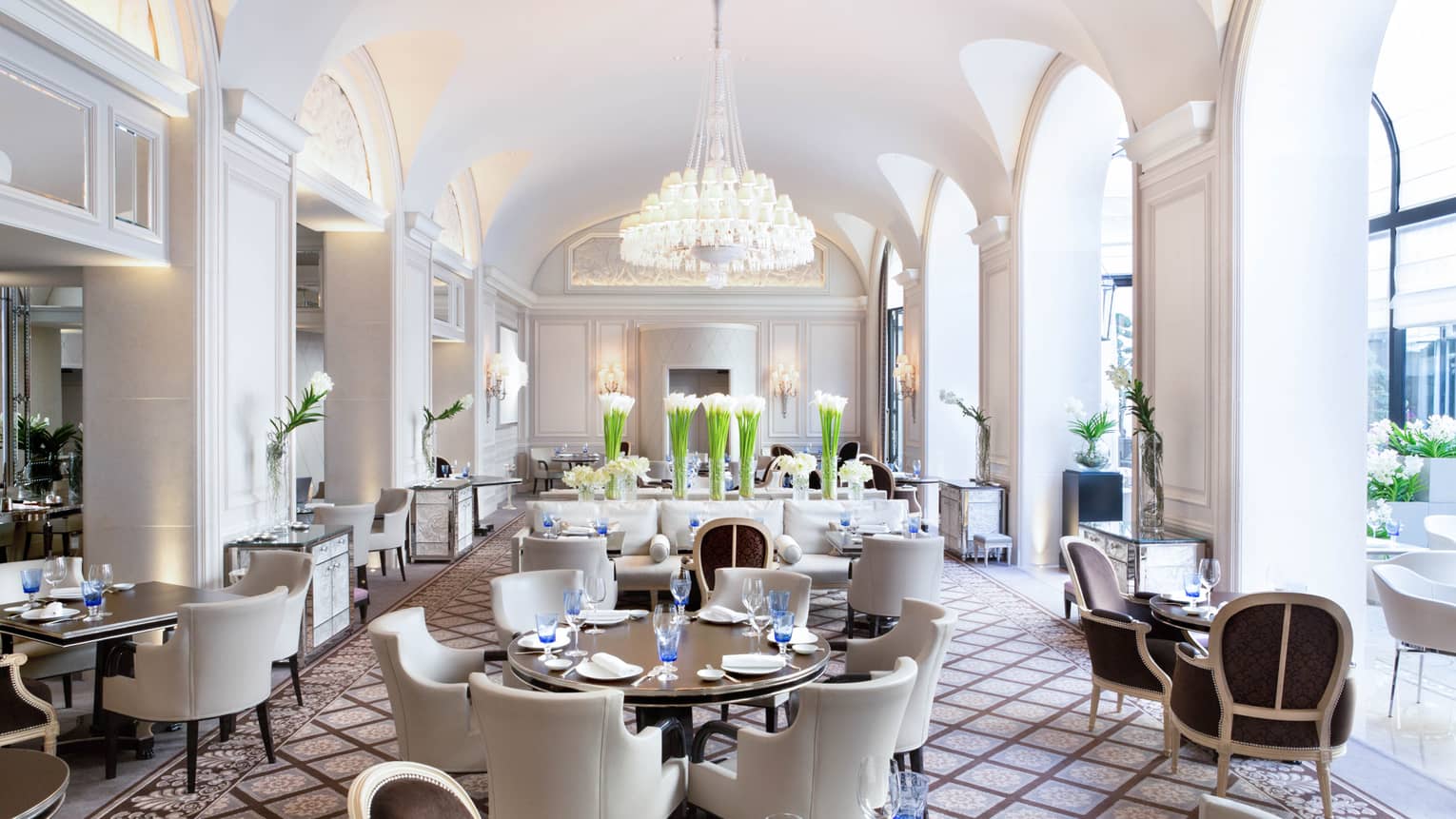 Bright Le George dining room, white chairs around tables under arched pillows, chandeliers