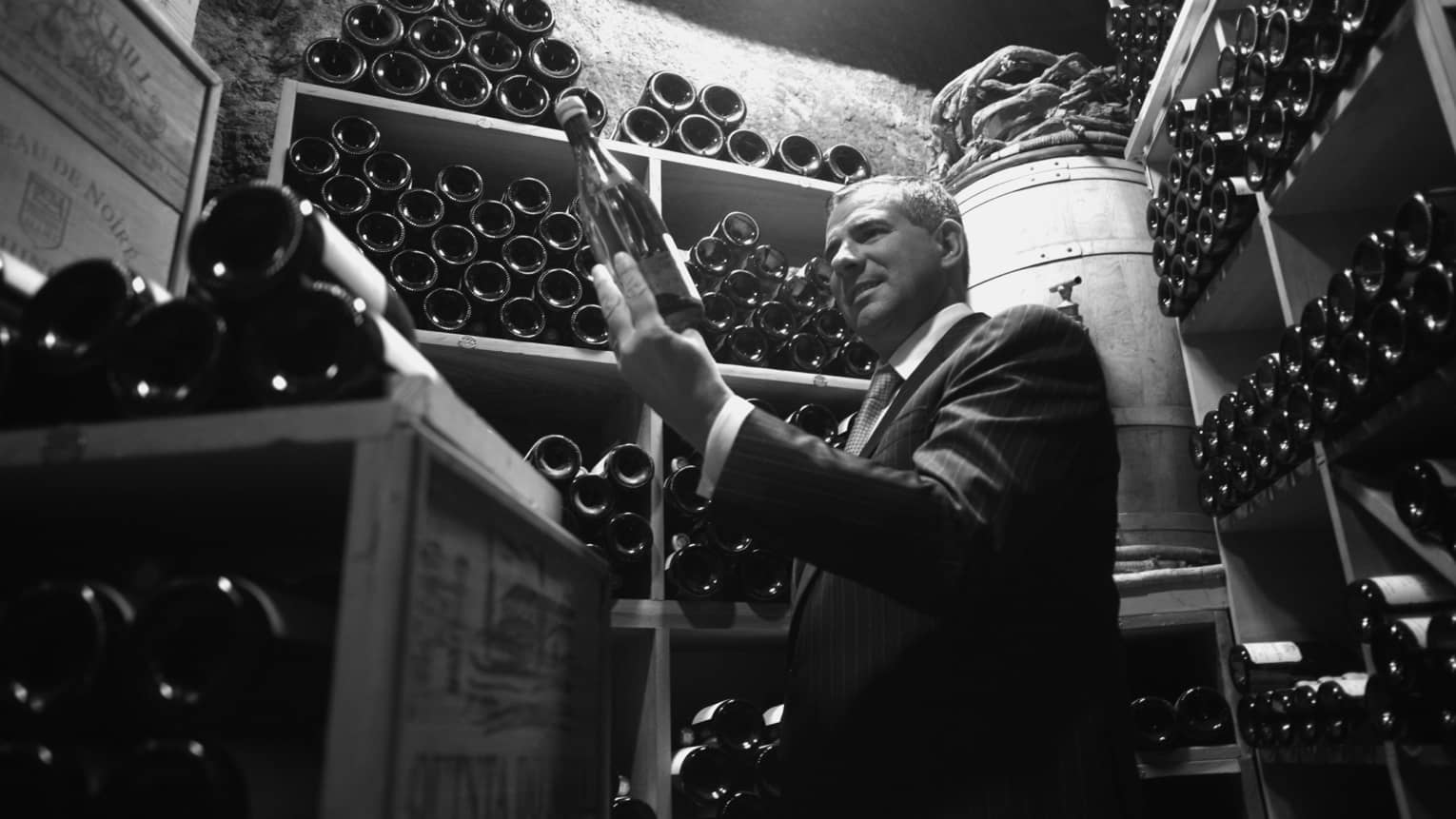Black and white photo of wine sommelier selecting bottle from cellar